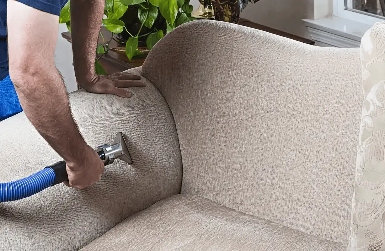 Professional upholstery cleaner deep-cleaning a fabric sofa with a handheld extraction tool and hose, Seattle, WA.